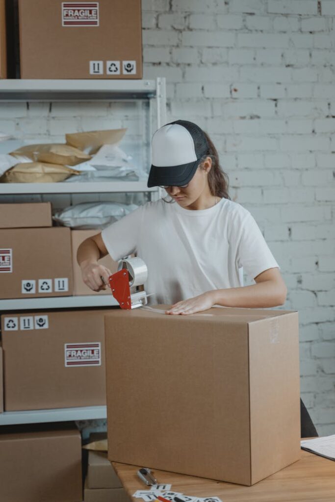 pexels photo 6169030 Young female worker sealing cardboard boxes in an indoor warehouse setting.