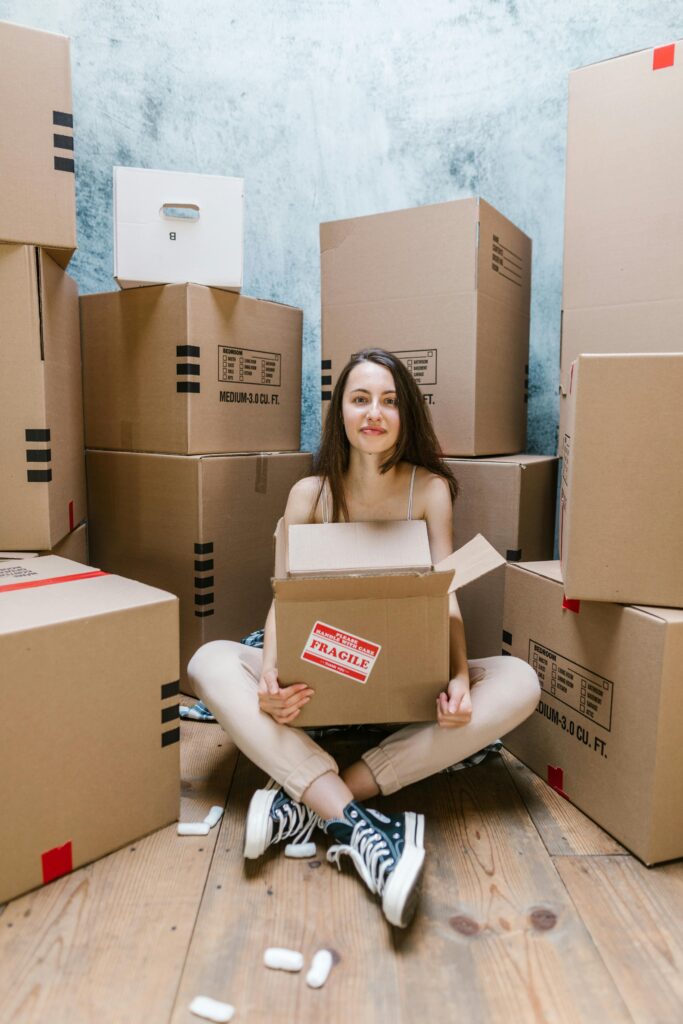 Woman sitting among boxes, packing belongings in a new home, contemplating relocation.
